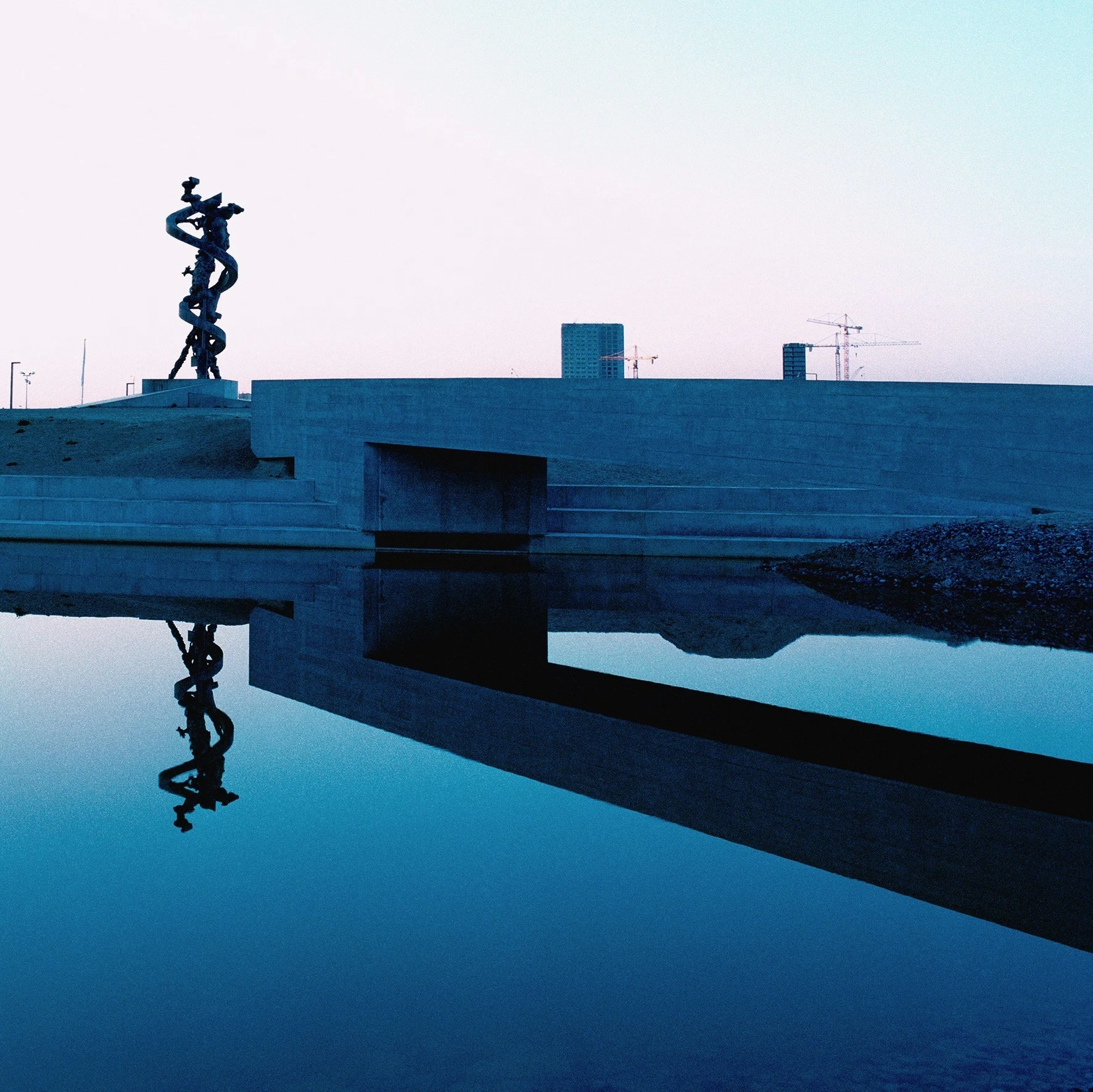 Sculpture reflected in water beside a concrete structure